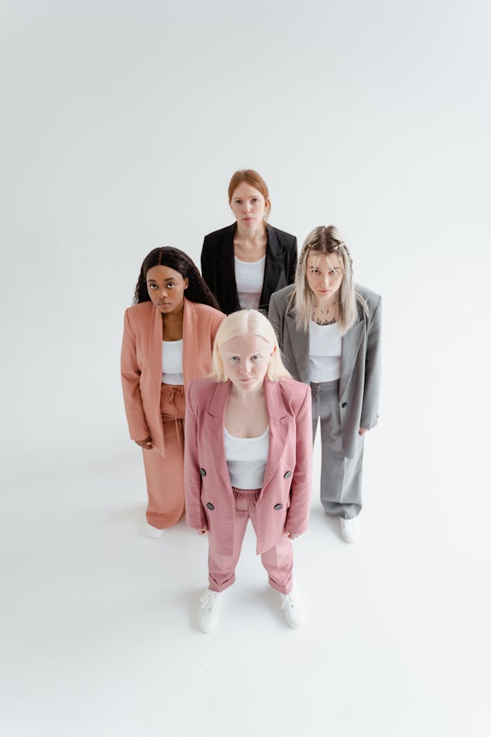 Four diverse women in modern suits, standing confidently in a studio with a white background.